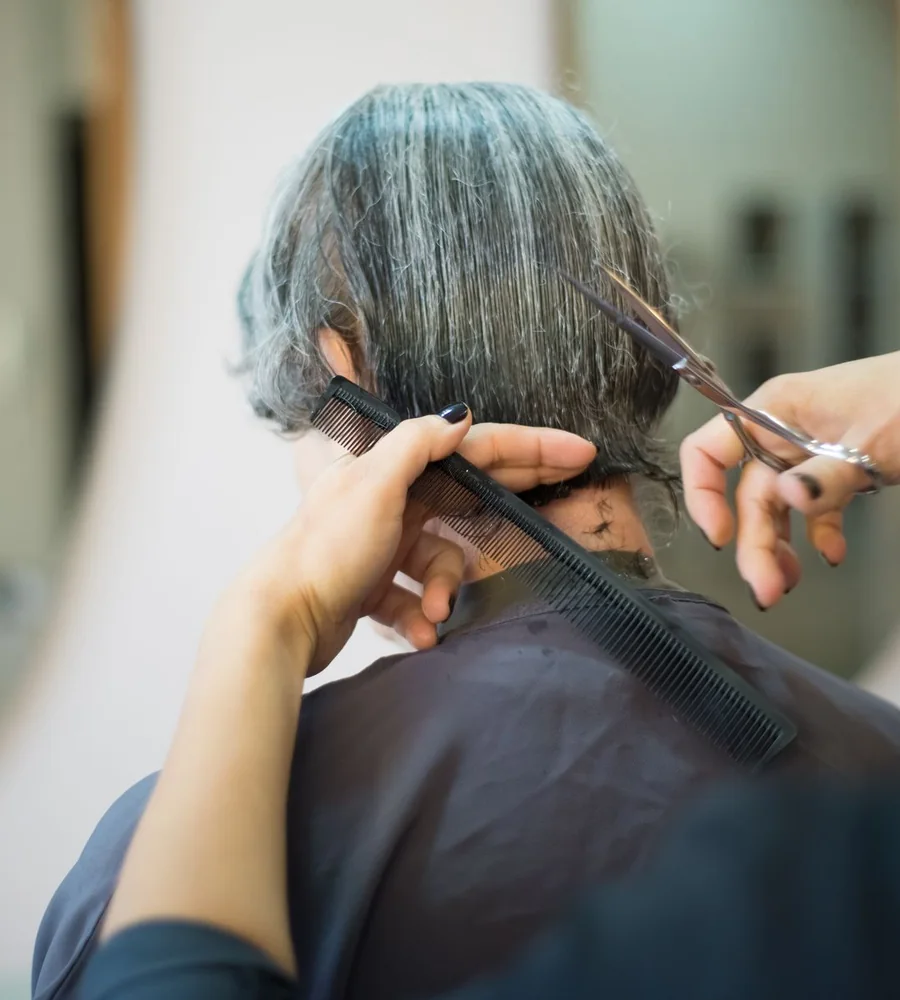 A hairdresser carefully trimming the back of a client’s short haircut